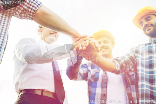 Image of close up of builders in hardhats with hands on top