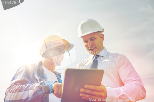 Image of happy builders in hardhats with tablet pc outdoors