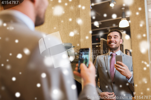 Image of man in suit taking mirror selfie at clothing store