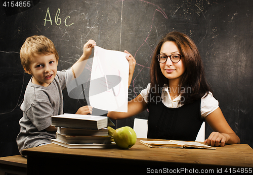 Image of little cute boy with young teacher in classroom studying at blac