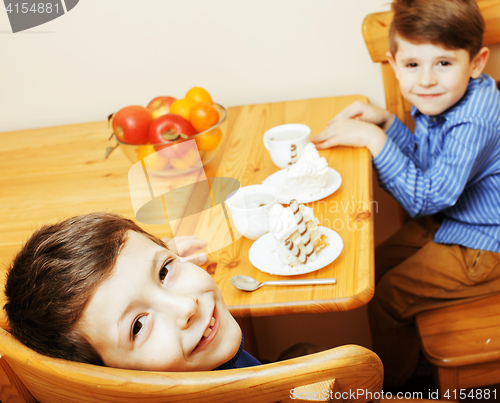 Image of little cute boys eating dessert on wooden kitchen. home interior