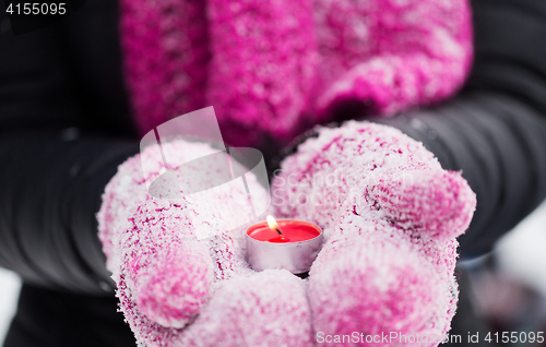 Image of close up of hands in winter mittens holding candle