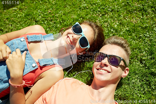 Image of happy teenage couple with earphones lying on grass