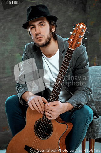 Image of Cool guy sitting with guitar on gray background