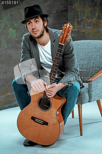 Image of Cool guy sitting with guitar on gray background