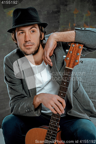 Image of Cool guy sitting with guitar on gray background
