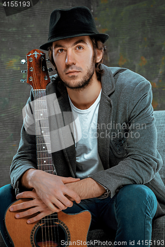 Image of Cool guy sitting with guitar on gray background