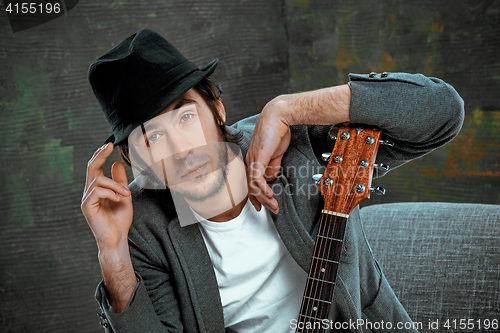 Image of Cool guy sitting with guitar on gray background