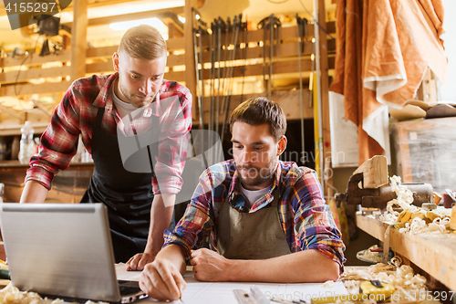 Image of carpenters with laptop and blueprint at workshop