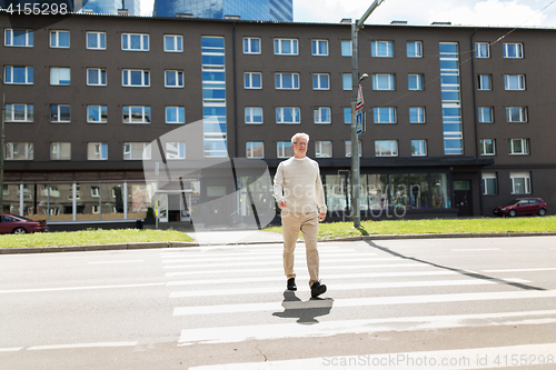 Image of senior man walking along city crosswalk