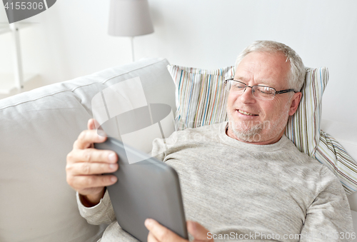 Image of senior man with tablet pc lying on sofa at home