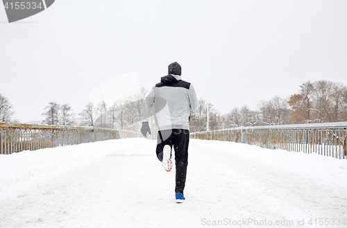 Image of man running along snow covered winter bridge road