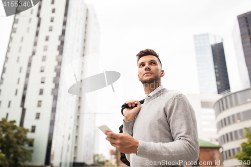 Image of young man with bag and smartphone in city