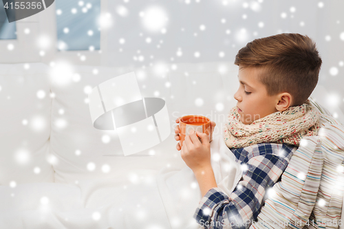 Image of ill boy with flu in scarf drinking tea at home