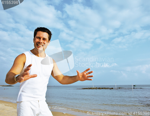 Image of young brunette man on beach at sea smiling, gomosexual in white 