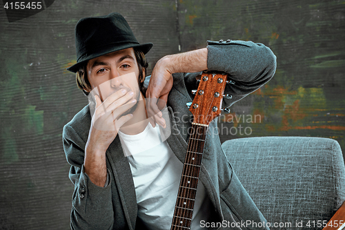 Image of Cool guy sitting with guitar on gray background