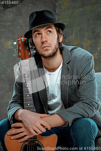 Image of Cool guy sitting with guitar on gray background