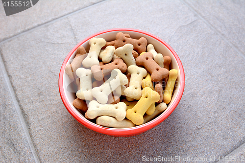 Image of Red bowl full of dog biscuits on grey tile