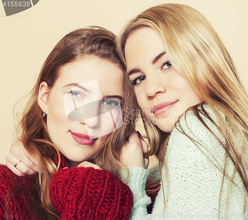 Image of Two young girlfriends in winter sweaters indoors having fun. Lifestyle. Blond teen friends close up