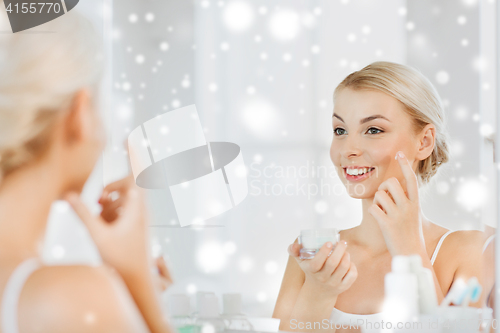 Image of happy woman applying cream to face at bathroom