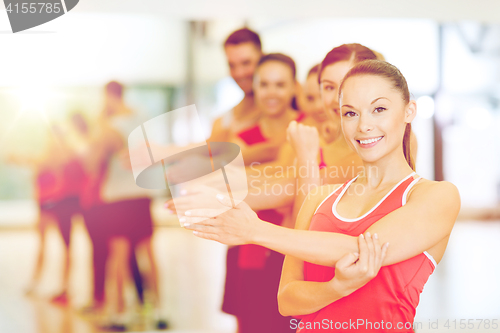 Image of group of smiling people stretching in the gym