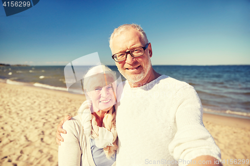 Image of seniors taking picture with selfie stick on beach