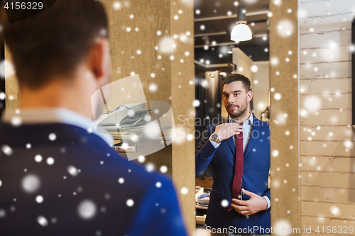 Image of man trying tie on at mirror in clothing store