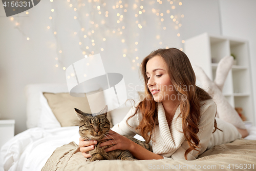 Image of happy young woman with cat lying in bed at home