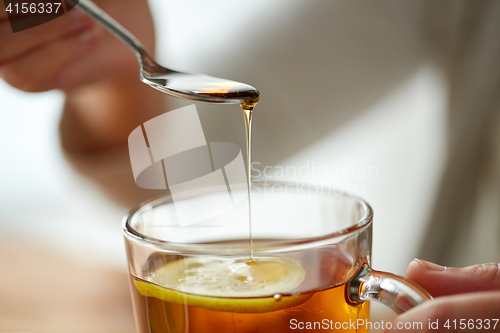 Image of close up of woman adding honey to tea with lemon