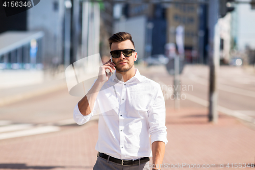 Image of happy man with smartphone calling on city street