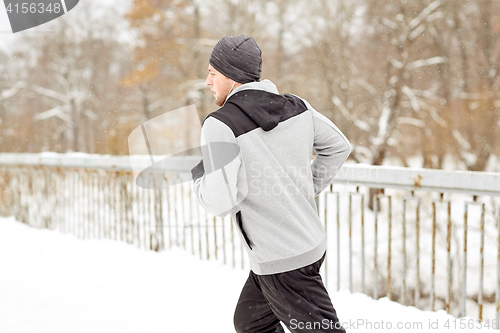 Image of man in earphones running along winter bridge