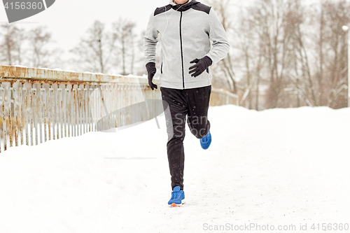 Image of man in earphones running along winter bridge