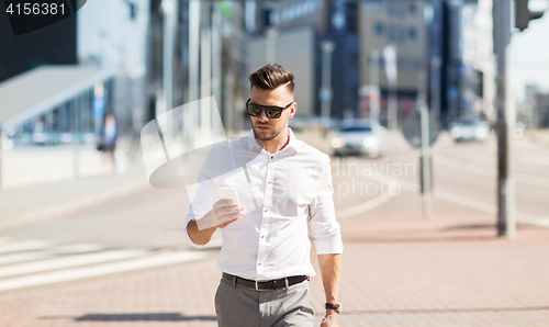 Image of man in sunglasses with smartphone walking at city