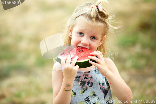 Image of Adorable blonde girl eats a slice of watermelon outdoors