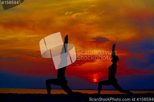 Image of Yoga people training and meditating in warrior pose outside by beach at sunrise or sunset.