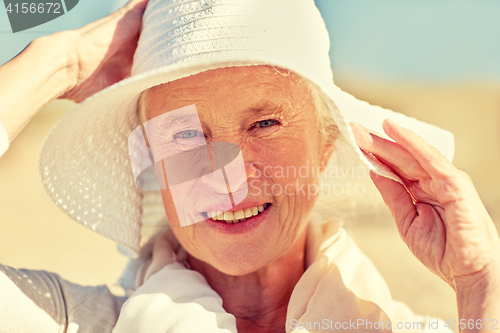 Image of happy senior woman in sun hat on summer beach