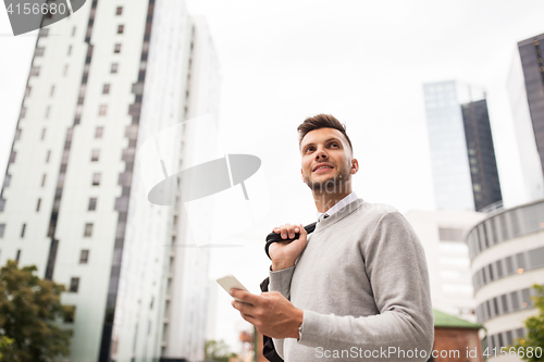 Image of happy young man with bag and smartphone in city