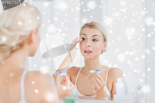 Image of young woman putting on contact lenses at bathroom