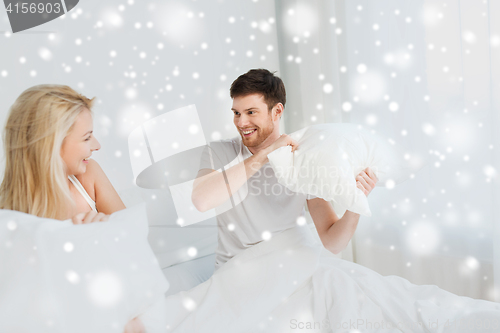 Image of happy couple having pillow fight in bed at home