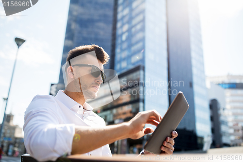 Image of man with tablet pc sitting on city street bench