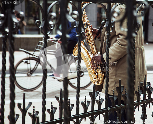 Image of african street musician playing jazz on saxophone throw lattice 