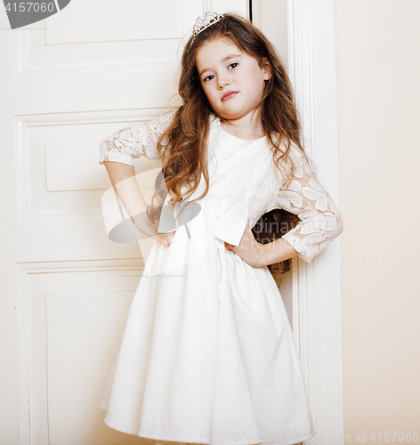 Image of little cute girl at home, opening door well-dressed in white dre