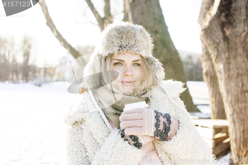 Image of young pretty teenage hipster girl outdoor in winter snow park having fun drinking coffee, warming up happy smiling, lifestyle people concept