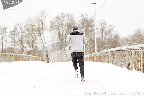 Image of man running along snow covered winter bridge road