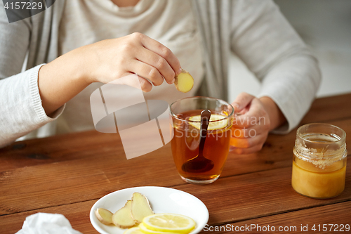 Image of close up of woman adding ginger to tea with lemon