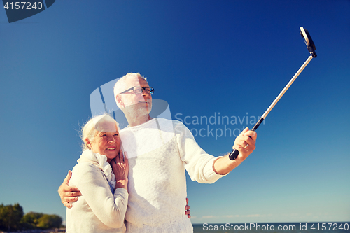 Image of seniors with smartphone taking selfie on beach