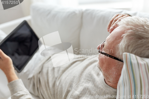 Image of senior man with tablet pc lying on sofa at home