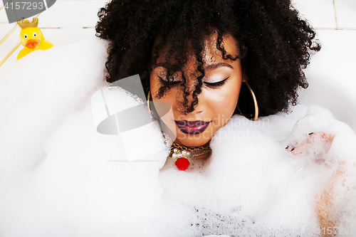 Image of young afro-american teen girl laying in bath with foam, wearing 