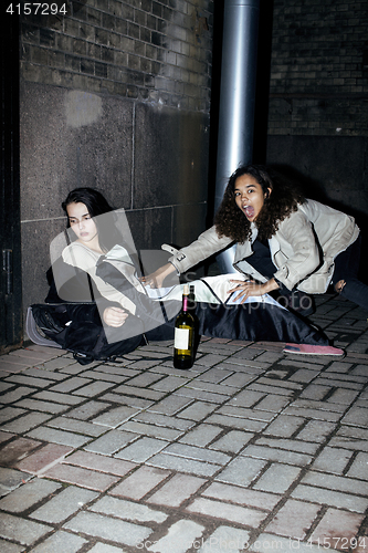 Image of young poor ttenage girl sitting at dirty wall on floor with bottle of vine, poor refugee alcoholic, hopeless homeless woman in depression, real junky concept