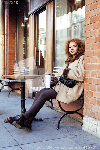 Image of young pretty african american women drinking coffee outside in c